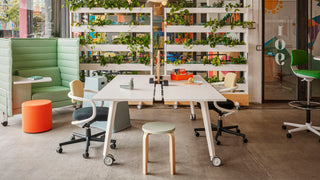 Sfeerbeeld van een kantoor met witte bureaus, plantenrek en een groene Vitra Alcove