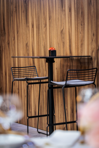 Sfeerbeeld van Flexfurn Wire barstoelen met kussen aan een statafel voor een houten wand