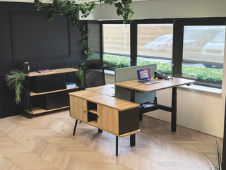 Alto elektrisch zit-sta bureau in eikendecor met zwart onderstel in hoogste stand, met scheidingswand en dressoir in een kantoor met visgraatparket