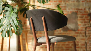 Detail van een donkere houten Mobitec Toro stoel met grijze zitting voor een bakstenen muur