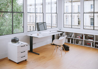 Photo d'ambiance d'un caisson Buronomic Comfort blanc sous un bureau noir près de grandes fenêtres