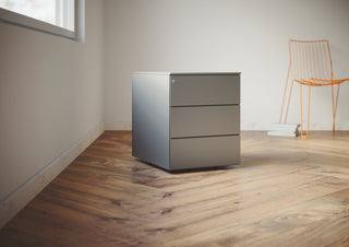 Lifestyle image of a Buronomic Paisible three-drawer metal pedestal in aluminium on a parquet floor